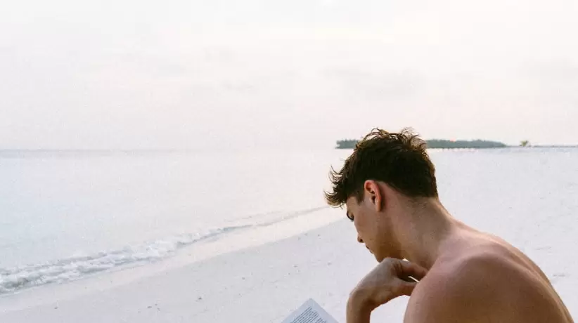 Libro De Lectura De Hombre En Topless Mientras Está Sentado En La Playa