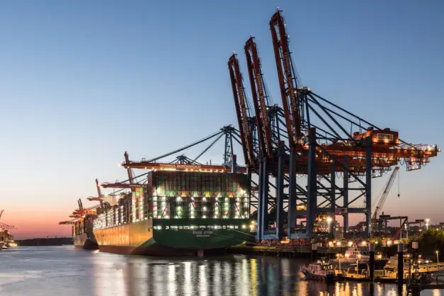 Un gran barco portacontenedores en el puerto de Hamburgo con grúas durante el crepúsculo, mostrando el comercio global. (Foto: Pexels)