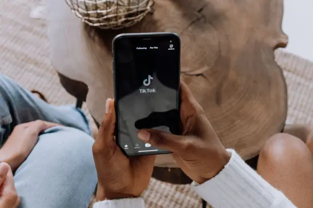 Primer plano de manos sosteniendo un smartphone que muestra la interfaz de la aplicación TikTok sobre una superficie de madera. (Foto: Pexels)