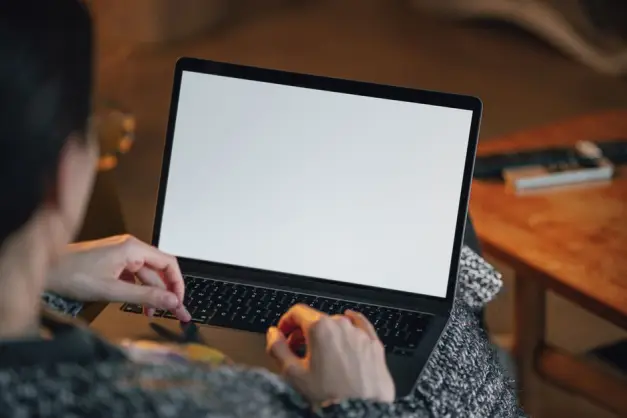 Persona trabajando de forma remota con un portátil en el regazo, pantalla en blanco visible. (Foto: Pexels)