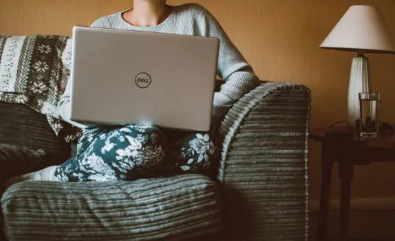 Una mujer con ropa casual trabaja en un portátil mientras se relaja en un sofá acogedor en el interior. (Foto: Pexels)