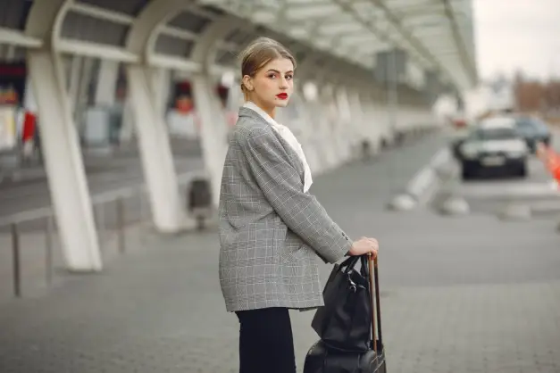 Mujer de negocios segura de sí misma de pie con equipaje al aire libre, lista para viajar. (Foto: Pexels)