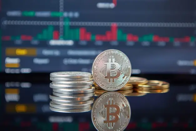 Pila de monedas de Bitcoin frente a un gráfico del mercado de valores, reflejando las tendencias de criptomonedas. (Foto: Pexels) - Foto: Pexels.