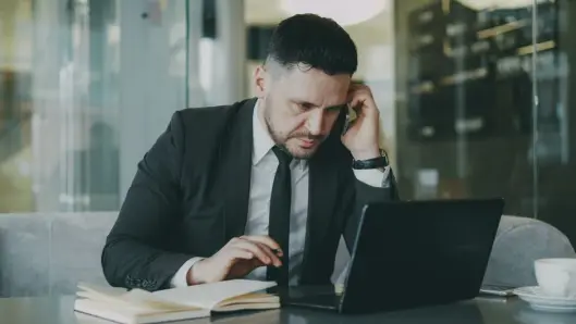 Empresario enfocado en traje multitasking en teléfono y laptop en oficina moderna. (Foto: Pexels)