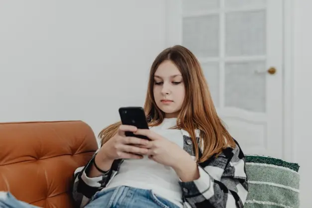 Chica adolescente usando el smartphone mientras se relaja en un sofá en interiores. (Foto: Pexels)