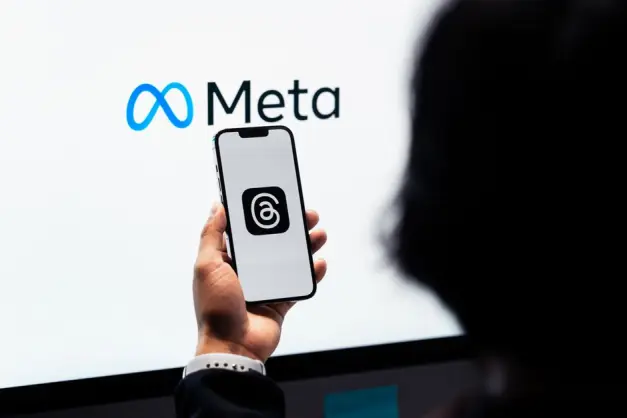 Manos sosteniendo un smartphone con el logo de Meta Threads en la pantalla, branding de Meta de fondo. (Foto: Pexels)