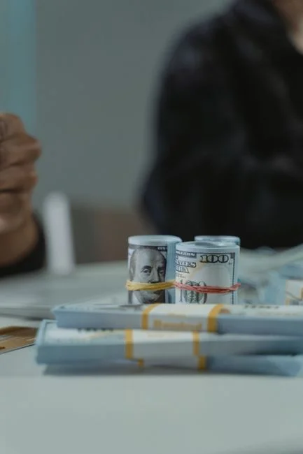 Primer plano de billetes de cien dólares estadounidenses enrollados y apilados en una mesa, perfecto para temas financieros.