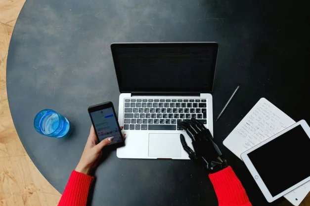 Una persona usando un laptop, smartphone y tablet con una mano protésica, enfatizando la conectividad digital.