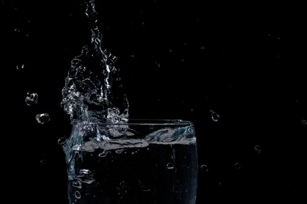 Primer plano de agua salpicando en un vaso contra un fondo negro.