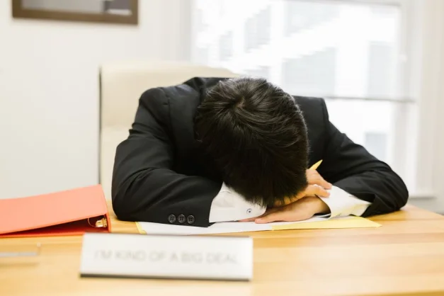 Persona de negocios durmiendo en un escritorio en una oficina, ilustrando la fatiga laboral.