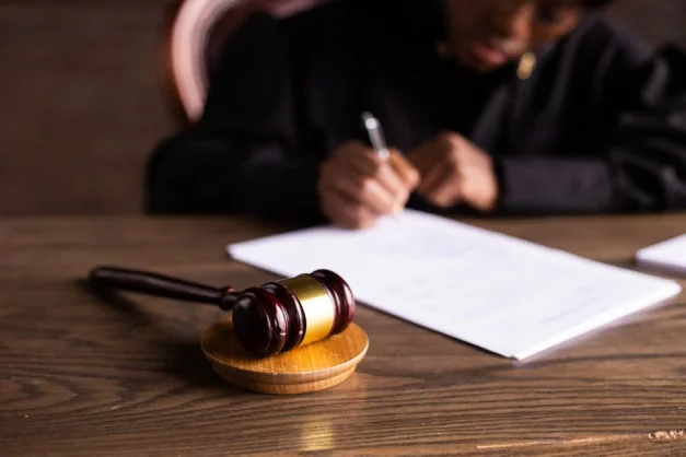 Juez firmando documentos en el escritorio con enfoque en el mazo, representando la ley y la justicia.