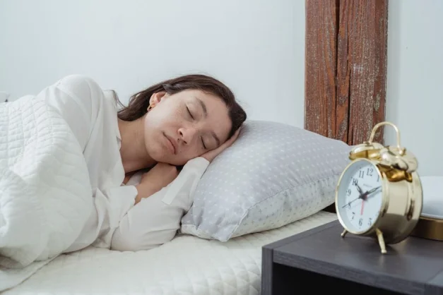 Joven mujer durmiendo pacíficamente en la cama con un reloj despertador vintage cerca.