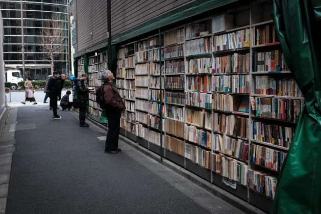 Estanterías de libros al aire libre en Tokio con personas explorando literatura en una calle de la ciudad.