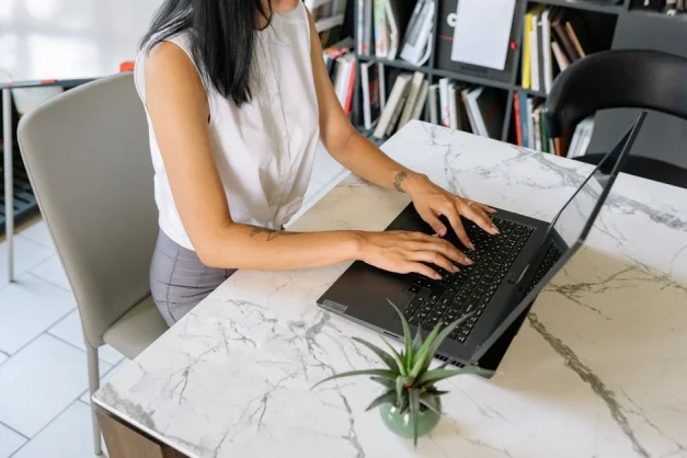 Una mujer profesional escribiendo en una computadora portátil en un entorno de oficina, con una mesa moderna de mármol.