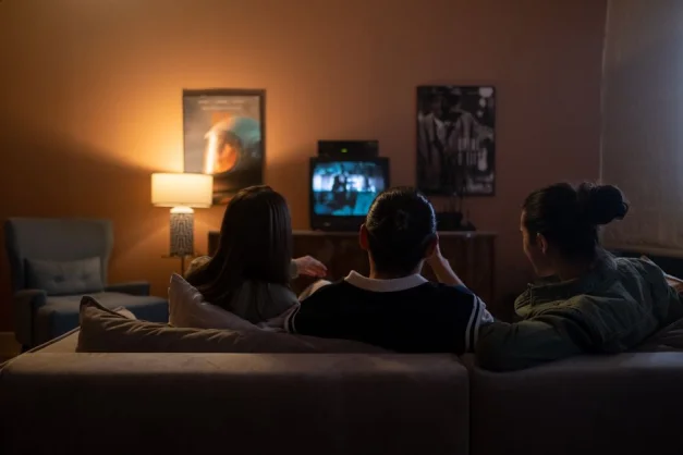 Tres personas disfrutando de una relajante noche de cine en casa, sentados en un sofá en una acogedora sala de estar.