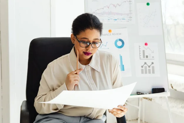 Mujer de negocios con gafas analizando documentos financieros en su escritorio.