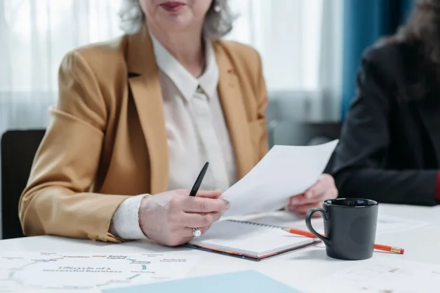 Una mujer mayor revisa documentos en una reunión de negocios, destacando profesionalismo.