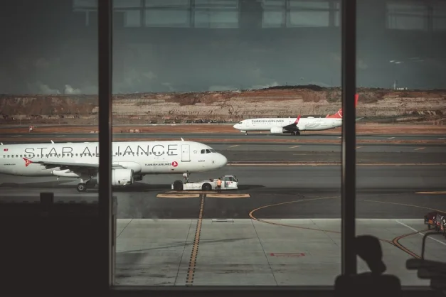 Una vista a través de las ventanas del aeropuerto que muestra aviones en la pista, creando un ambiente de viaje.