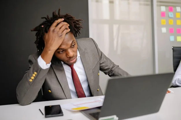 Empresario con rastas luciendo preocupado mientras trabaja en un portátil en la oficina.
