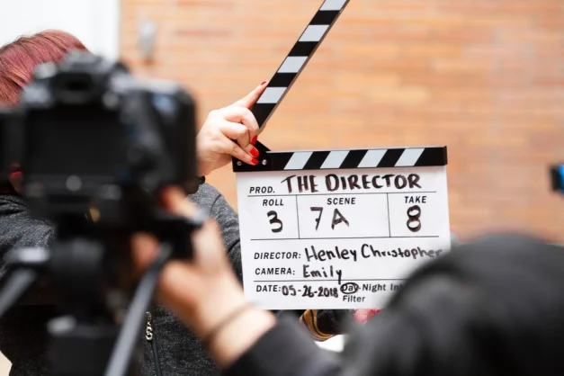 Primer plano de una pizarra de clapper de cine en acción con una cámara filmando una toma en el set.